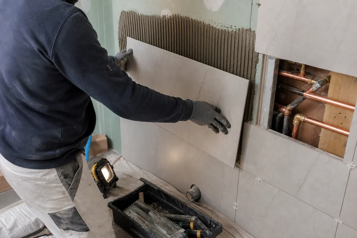 Artisan carreleur posant du carrelage grand format dans une salle de bain en rénovation, pavillon de Seine-et-Marne